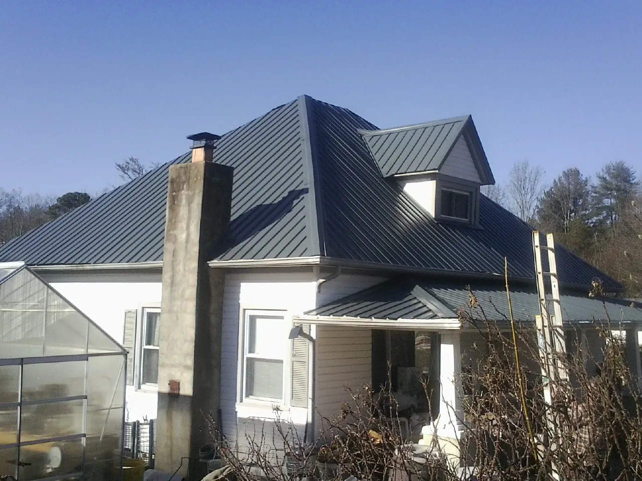 Dark blue standing seam metal roof on a white farmhouse with dormer — Slate & Tile Roof Repair by Roofing Brothers in Barksdale