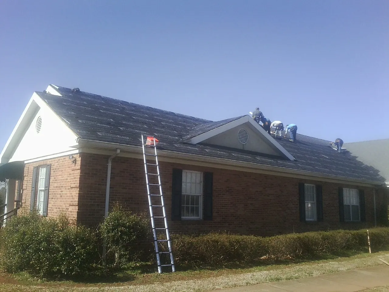 Crew tearing shingles off a brick ranch roof with a ladder set — Emergency Roof Repair work by our crew in Barksdale