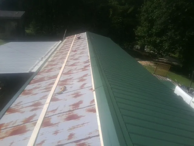 Old rusted panels beside newly installed green metal roofing — Wind Damage Roof Repair by Roofing Brothers in Barksdale