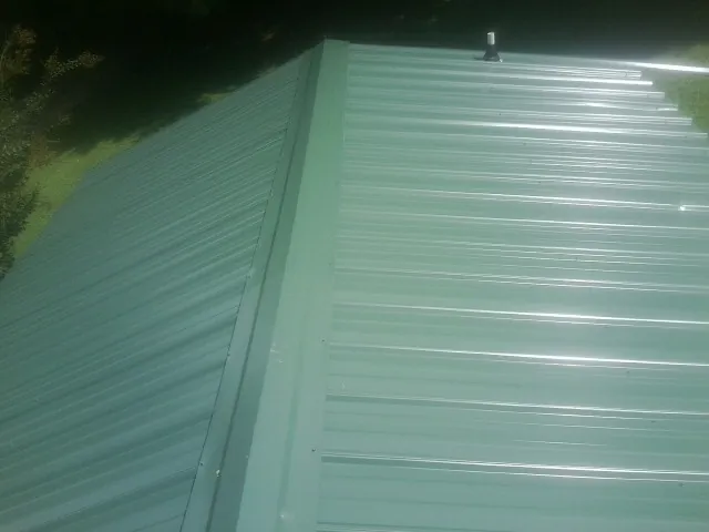New green metal panels meeting at the ridge of a roof — Flat Roof Repair work by our crew in Barksdale