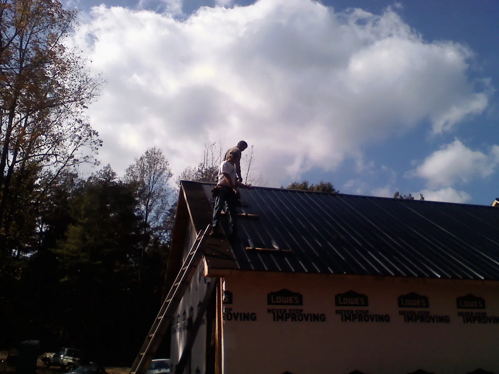 Roofer fastening dark metal panels high against a cloudy sky, from a Roof Inspection job in Barksdale