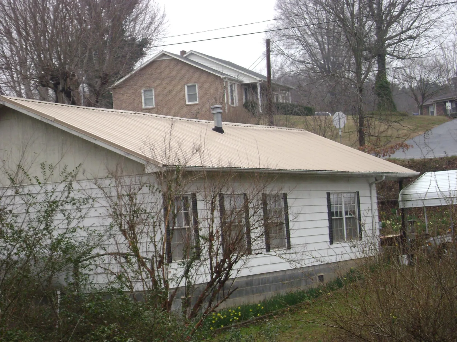 Tan metal roof on a white sided house set into a hillside — Commercial Roofing by Roofing Brothers in Barksdale